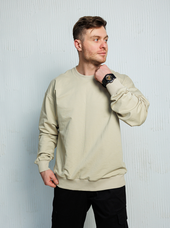 A fashionable and trendy man confidently strikes a pose while wearing a stylish beige sweatshirt and sleek black pants